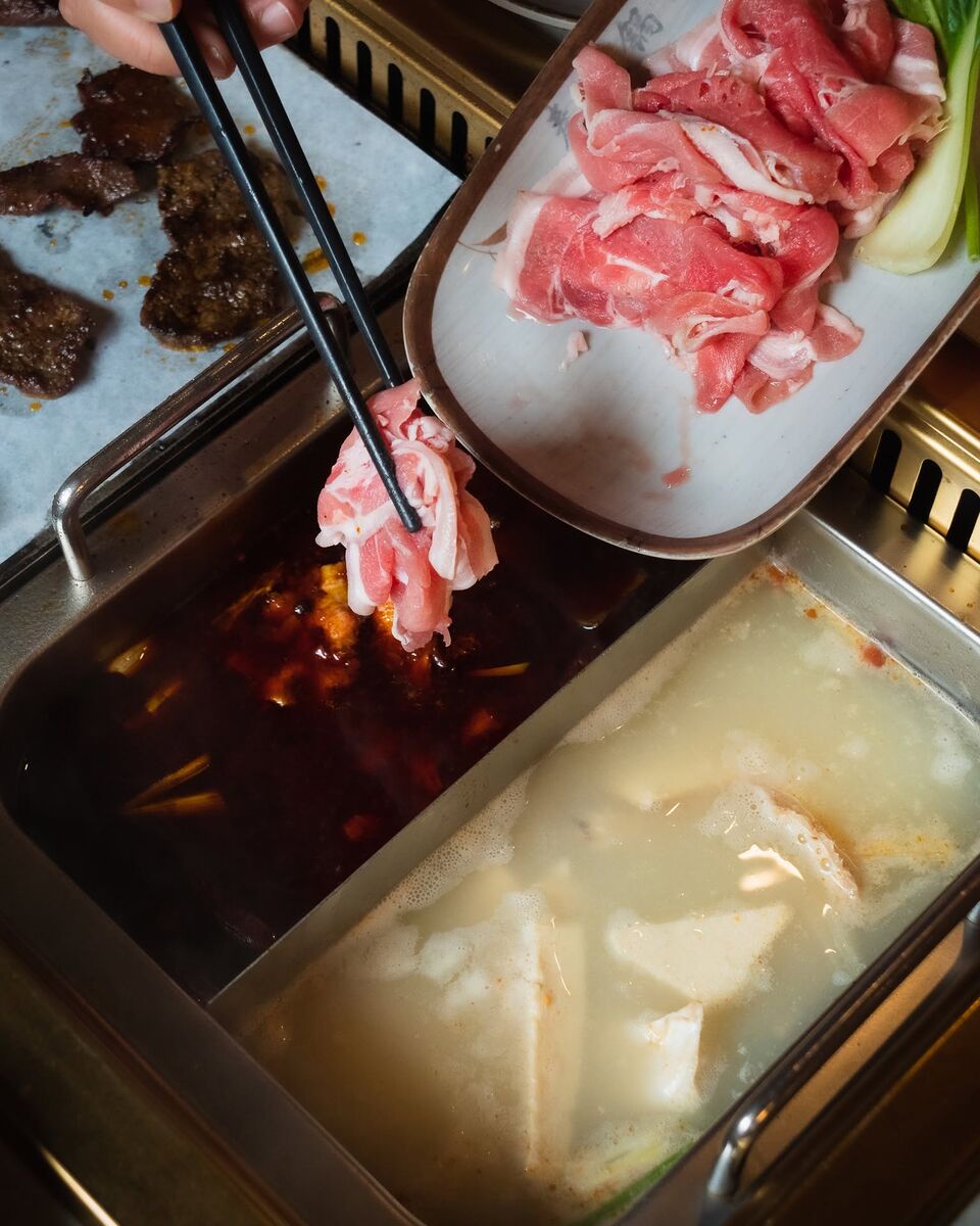 Chopsticks dipping rolled lamb into a split pot, red chilli broth on one side and milky bone broth on the other