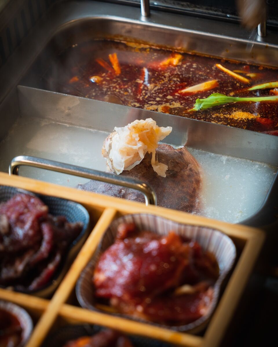 Crab cooking in the milky bone broth, the red chilli side behind and a tray of marinated meats in front