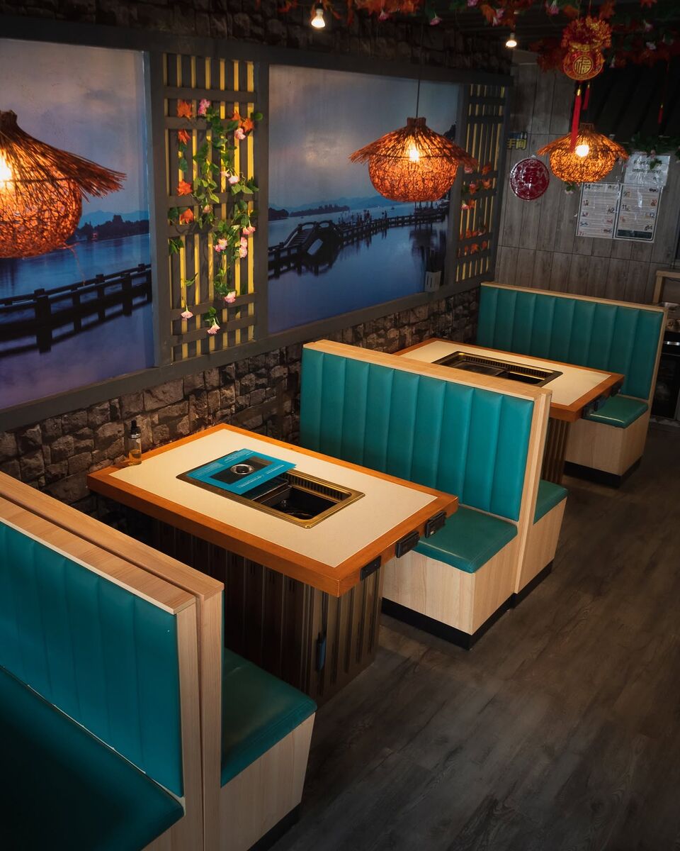 Booths beneath a blue lake-and-bridge mural, with lanterns and a backlit timber lattice
