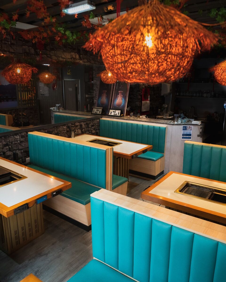 Teal booths and a woven rattan lantern in the foreground, the room glowing behind