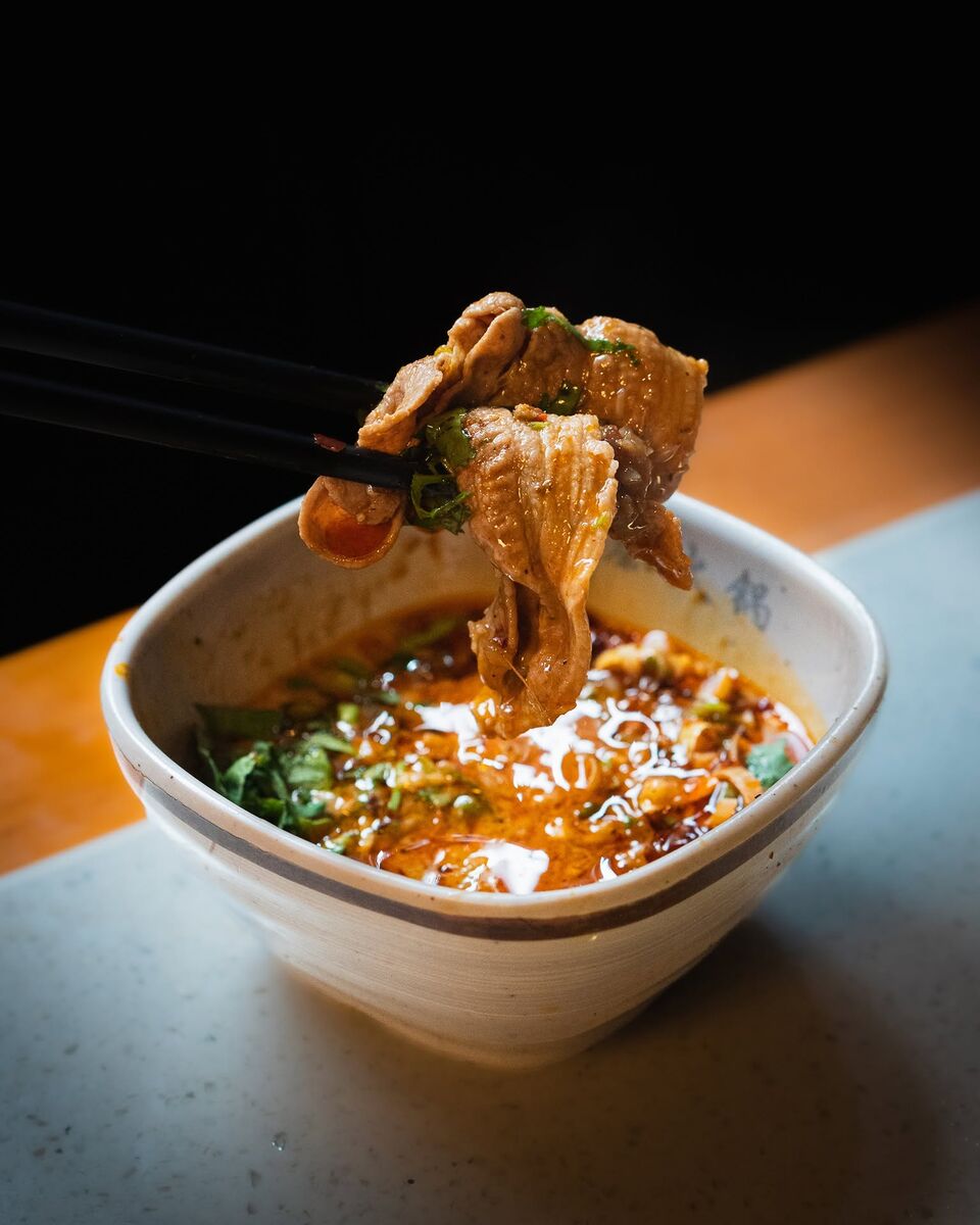 Cooked lamb lifted out of a bowl of chilli-oil dip