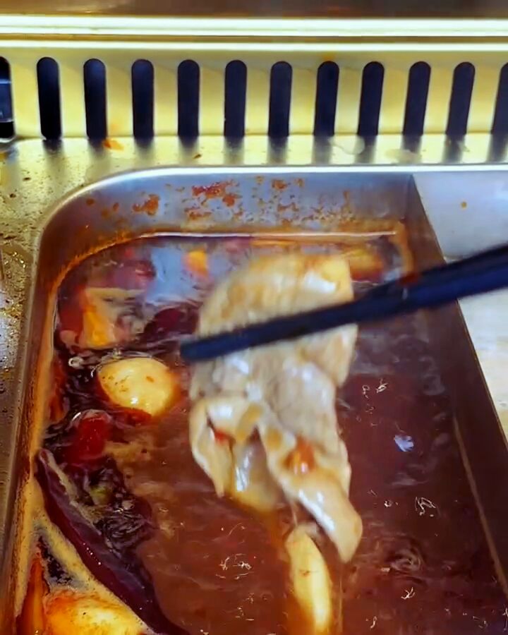 Chopsticks lifting cooked lamb out of the red chilli broth