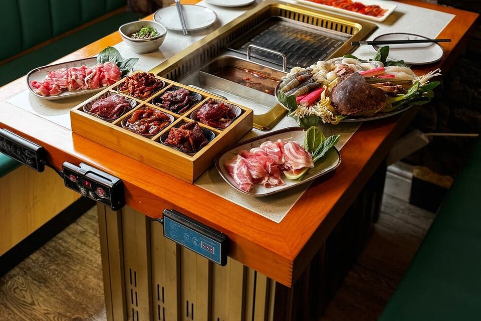 A full table: the split pot and grill plate, a nine-compartment tray of marinated meats, a seafood platter and plates of rolled meat